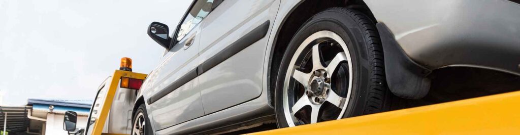 Abschleppen: Kaputtes Auto auf einem Pritschenabschleppwagen wird zur Reparatur transportiert