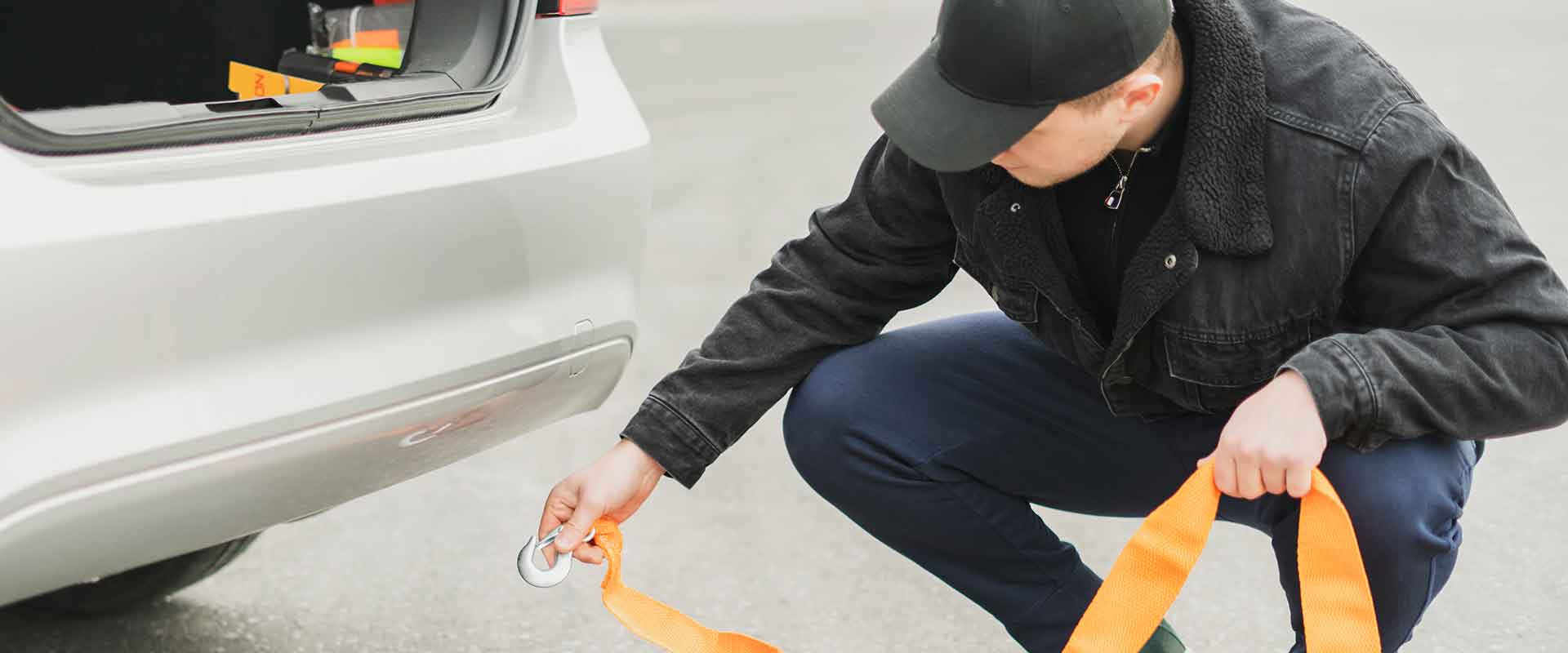 ein männlicher Fahrer befestigt das Seil am Abschlepphaken eines Autos