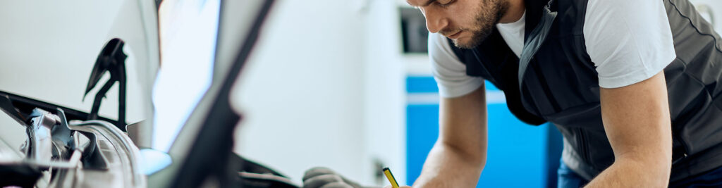Junger Mechaniker macht sich Notizen bei der Analyse des Automotors in der Autowerkstatt