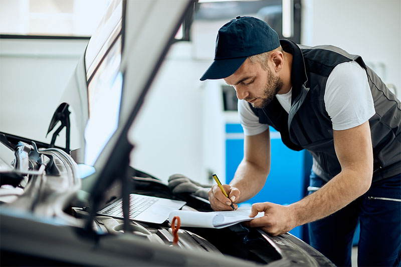 Junger Mechaniker macht sich Notizen bei der Analyse des Automotors in der Autowerkstatt