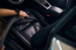 Mann reinigt ein Auto mit Staubsauger mit Fugendüse