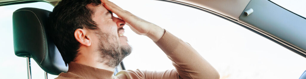 Schreckliche Schmerzgrimasse im Gesicht eines jungen Fahrers, eine Hand auf seiner Stirn, eine Grimasse im Gesicht