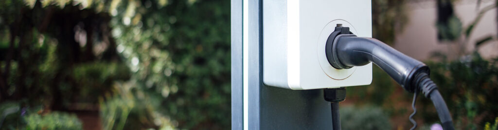 Inmitten einer üppigen Gartenanlage wurde eine Ladestation für Elektrofahrzeuge mit schwarzem Ladekabel installiert