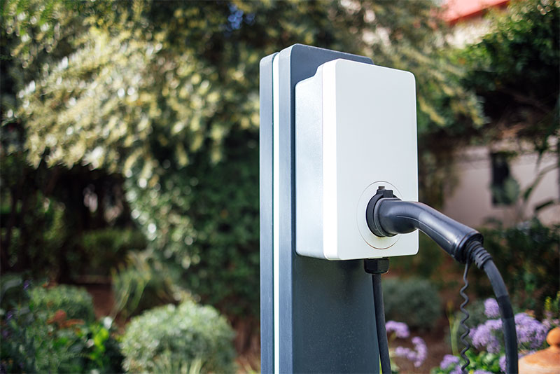 Inmitten einer üppigen Gartenanlage wurde eine Ladestation für Elektrofahrzeuge mit schwarzem Ladekabel installiert